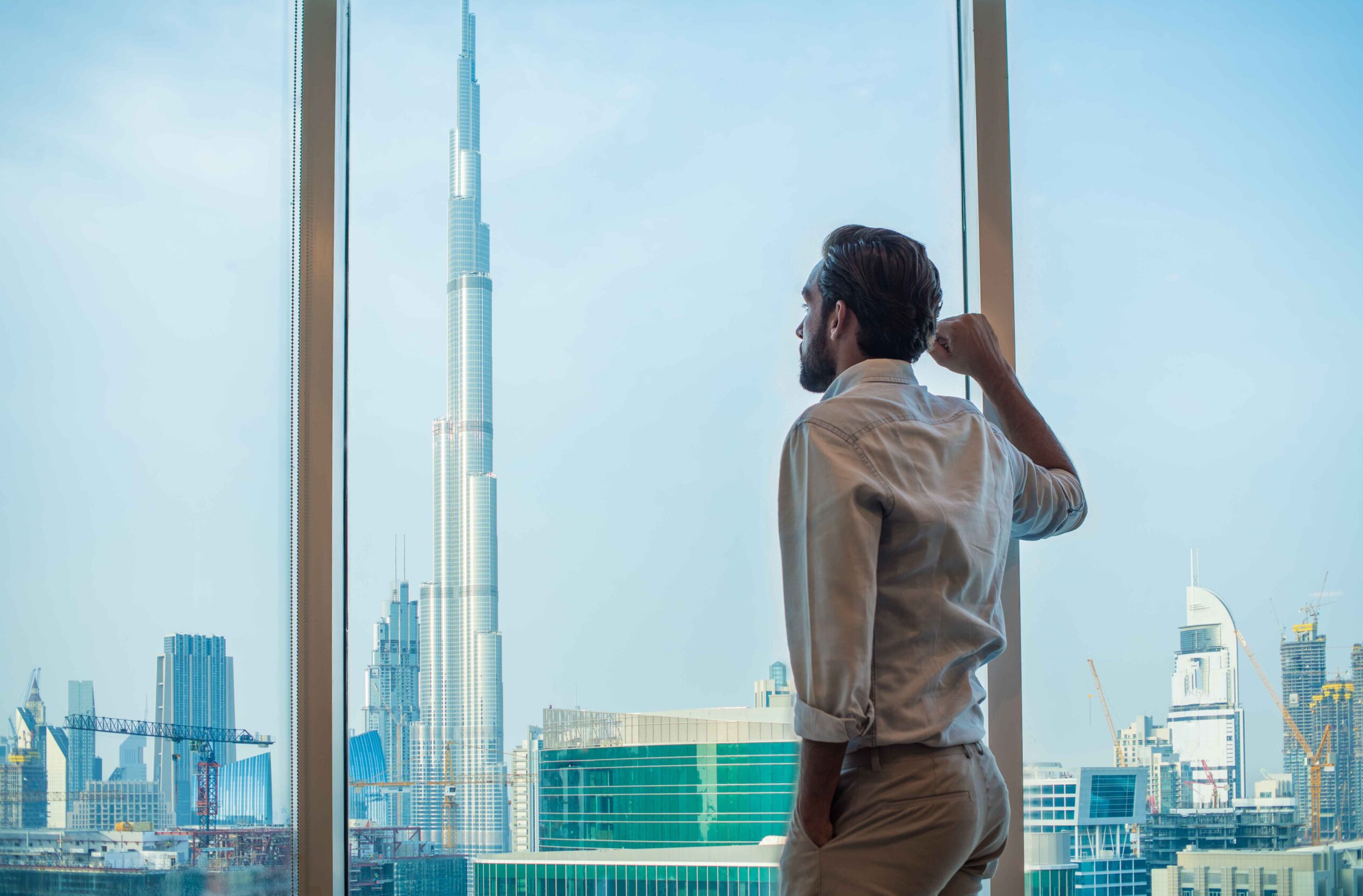 Businessman gazing out from a luxury Dubai residence at the Burj Khalifa skyline, symbolizing ambition, legacy, and future opportunity.